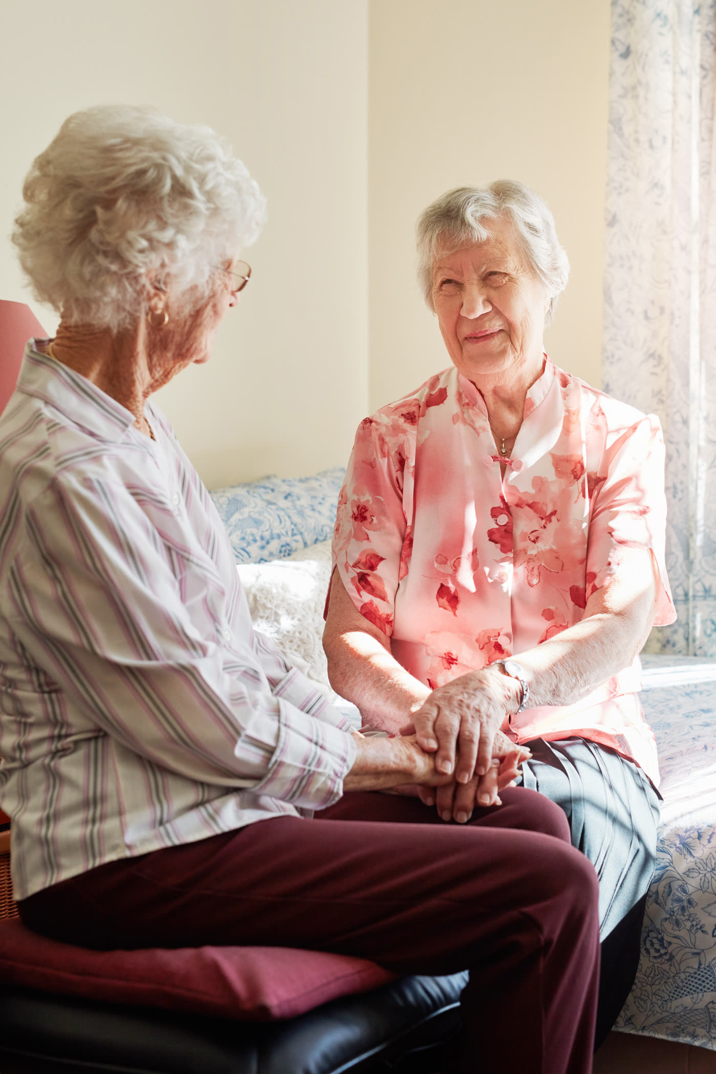 Two senior women sitting together, smiling and holding hands